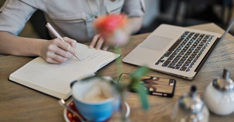 Content - Person Writing On A Notebook Beside Macbook