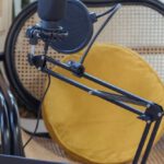 Podcast Equipment - Modern laptop and microphone on tripod placed near wicker chair in modern studio before recording podcast