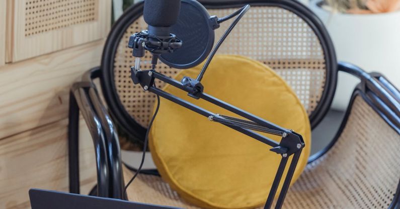 Podcast Equipment - Modern laptop and microphone on tripod placed near wicker chair in modern studio before recording podcast