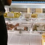 Payment Options - Back view of anonymous customer standing near glass showcase with assorted sweets while choosing delicious desserts in confectionery shop and making order