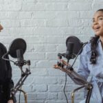 Podcast Formats - Smiling African American female guest gesticulating while having interview with journalist sitting near mic