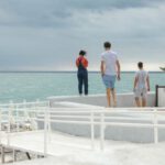 Features - Three People Standing on White Surface Near Body of Water