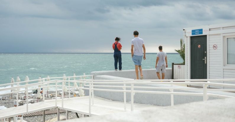 Features - Three People Standing on White Surface Near Body of Water