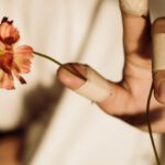 Organic Reach - From above of crop unrecognizable lady in fabric covering face reaching arm with medical patches on fingers with bright flowers on blurred background