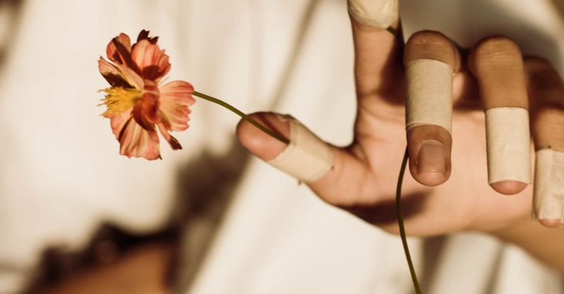 Organic Reach - From above of crop unrecognizable lady in fabric covering face reaching arm with medical patches on fingers with bright flowers on blurred background